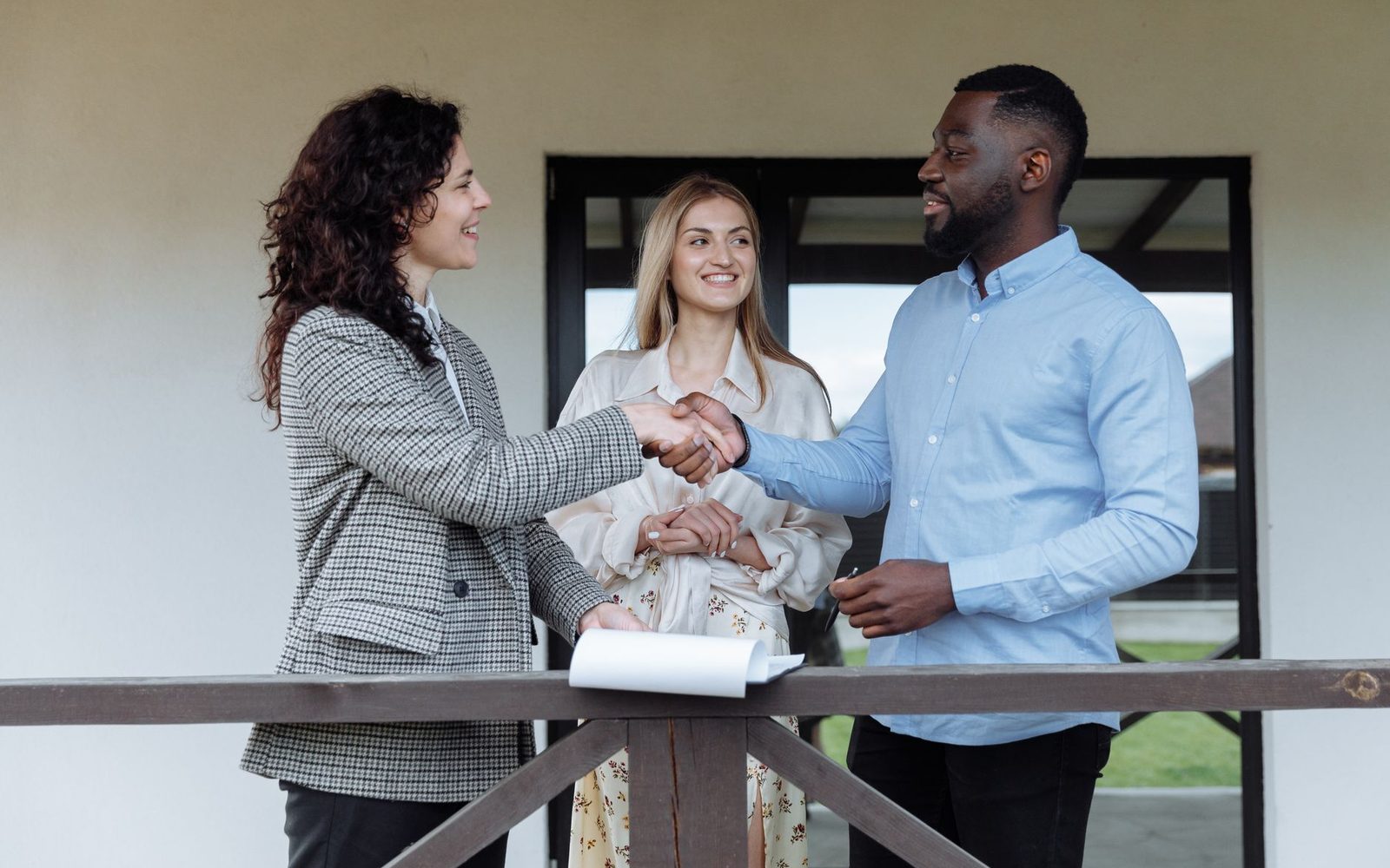 An agent shaking hands with clients on the porch of a home